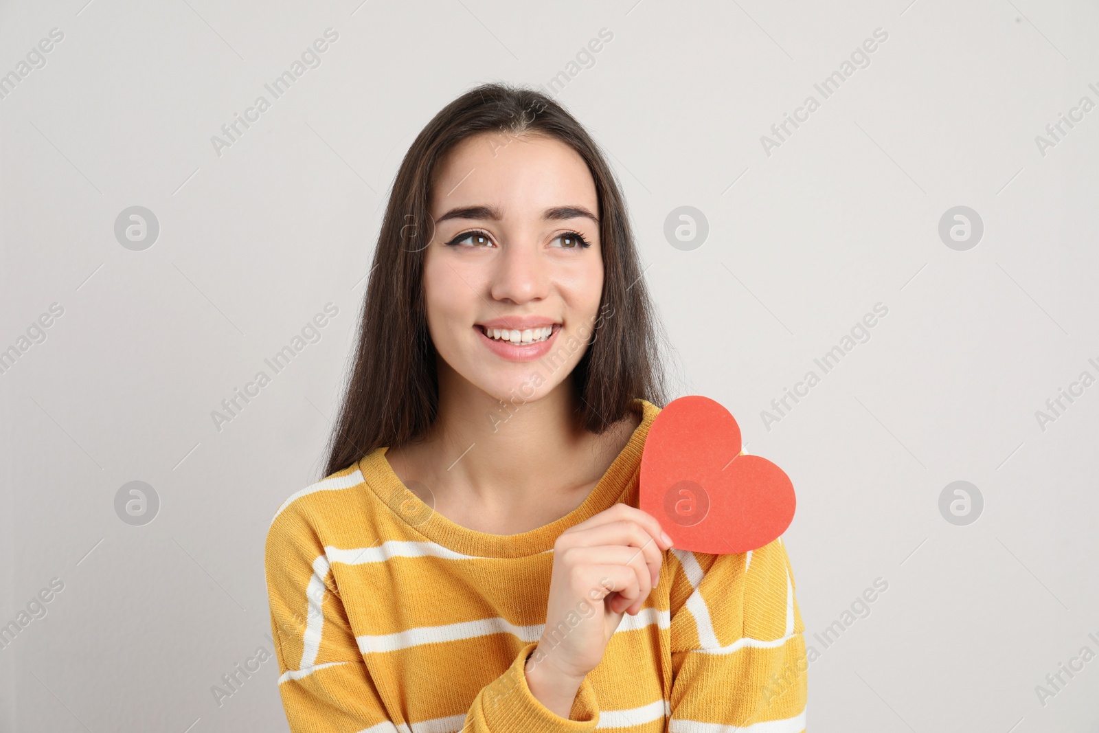 Photo of Portrait of beautiful young woman with paper heart on light background