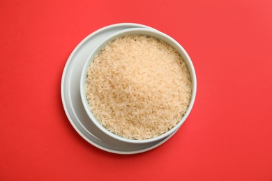 Photo of Bowl with uncooked rice on color background, top view