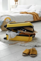 Photo of Open suitcase full of clothes, shoes and summer accessories on floor in room