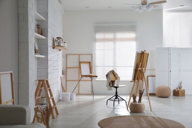 Photo of Modern studio interior with artist's workplace and foldable wooden easel near large window