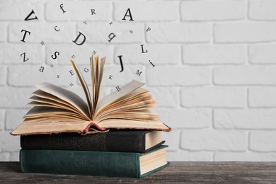 Image of Open book with letters flying out of it on wooden table, space for text