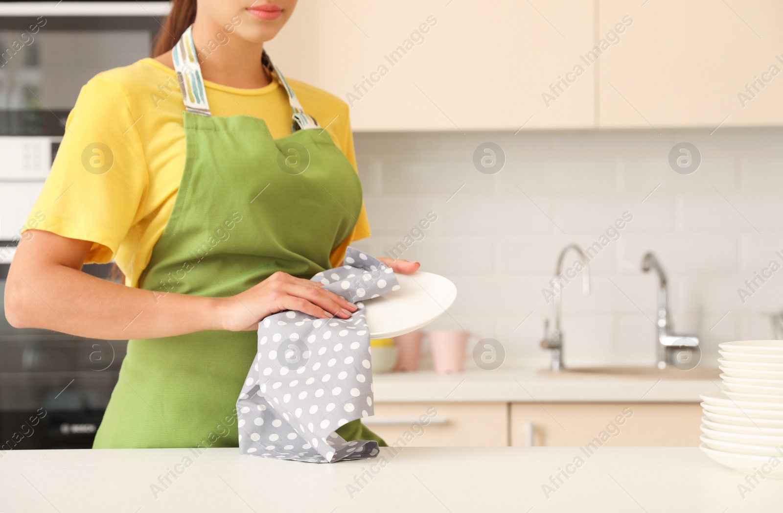 Photo of Young woman wiping clean plate in kitchen. Dish washing