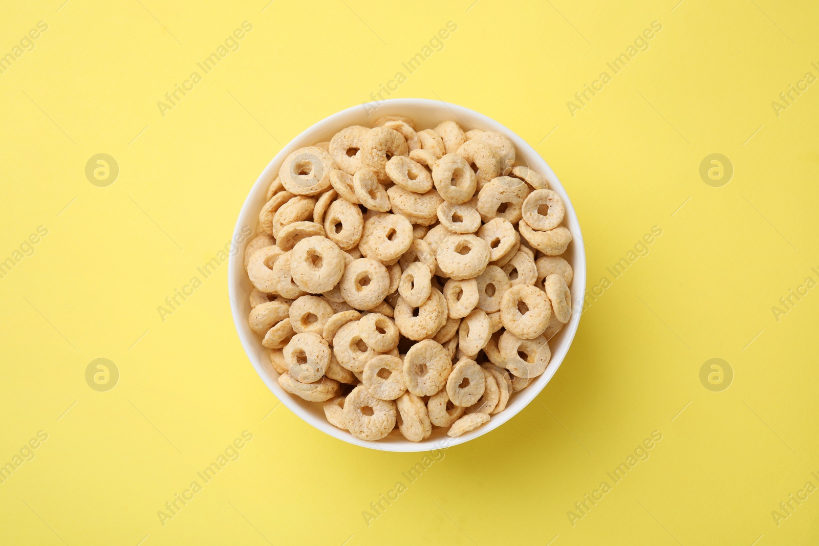 Photo of Tasty cereal rings in bowl on yellow table, top view