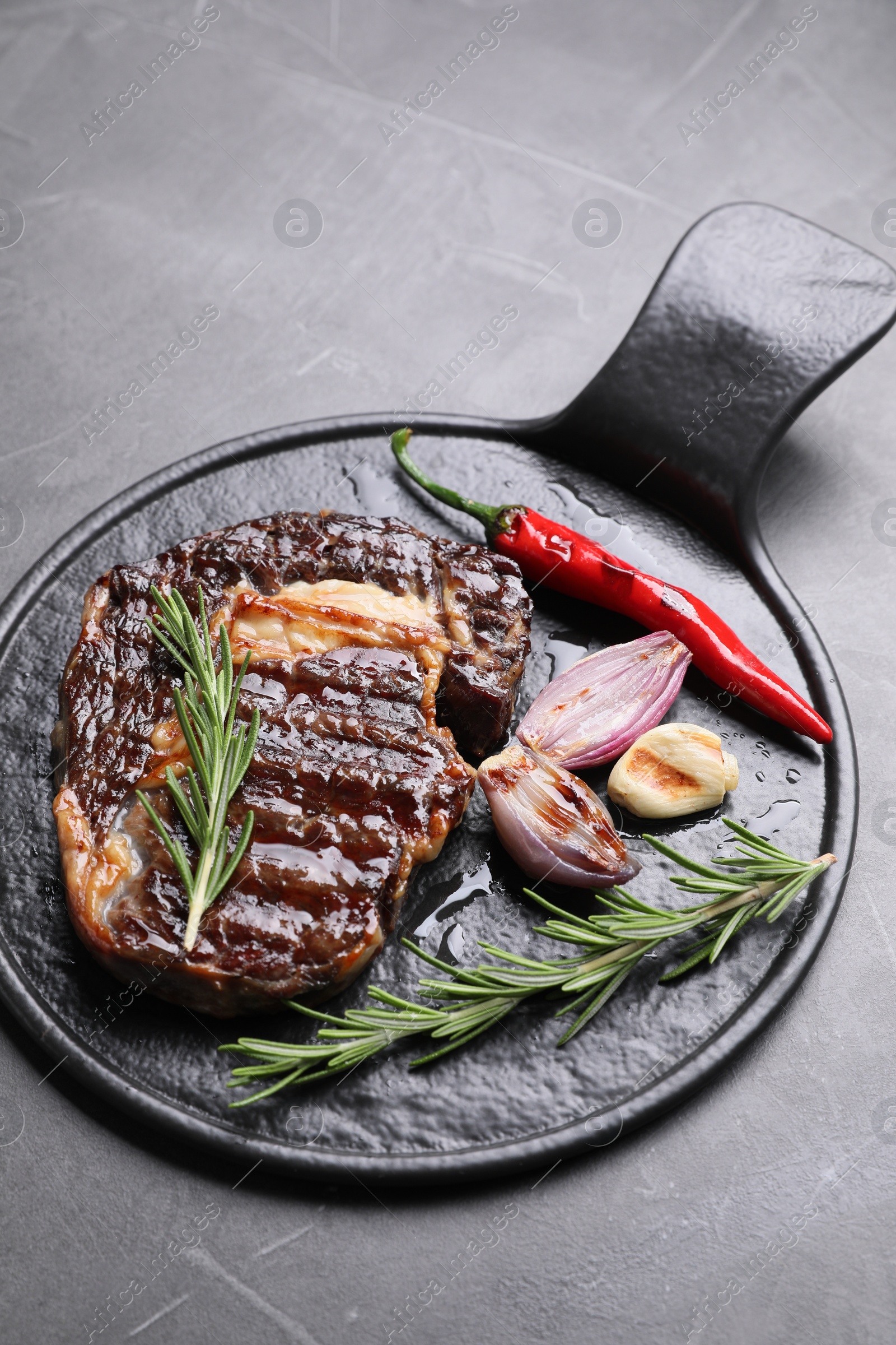 Photo of Delicious grilled beef meat, rosemary and spices on gray textured table, space for text