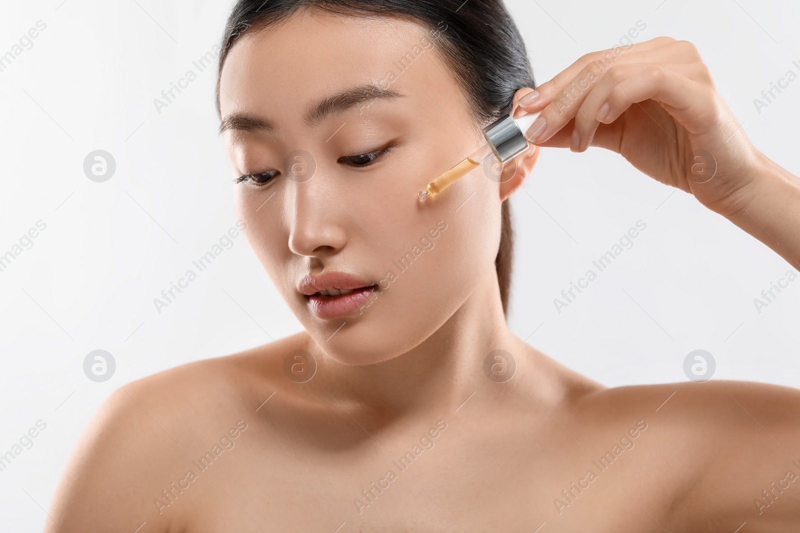 Photo of Beautiful young woman applying cosmetic serum onto her face on white background, closeup