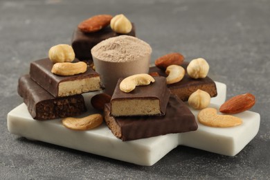 Photo of Different energy tasty bars, nuts and protein powder on grey table