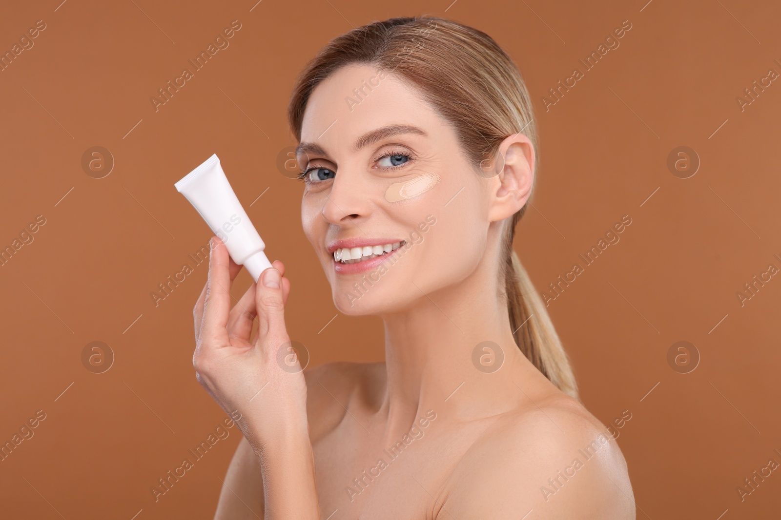Photo of Woman holding tube of foundation on brown background