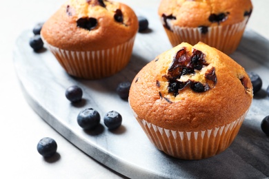 Stone board with blueberry muffins on light table, closeup view