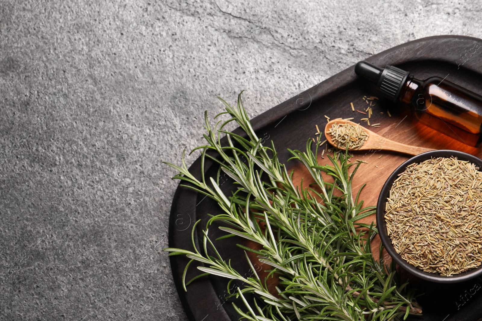 Photo of Bottle of essential oil, fresh and dry rosemary on grey table, top view. Space for text