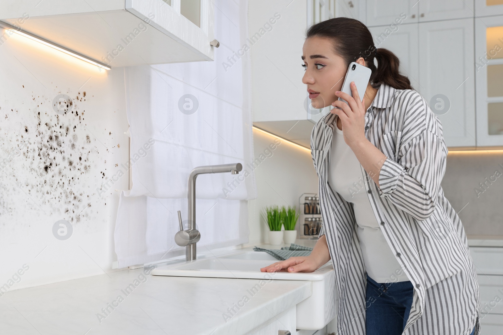 Image of Mold removal service. Woman talking on phone and looking at affected wall in kitchen