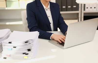 Photo of Female worker working with laptop near stack of documents in office, closeup
