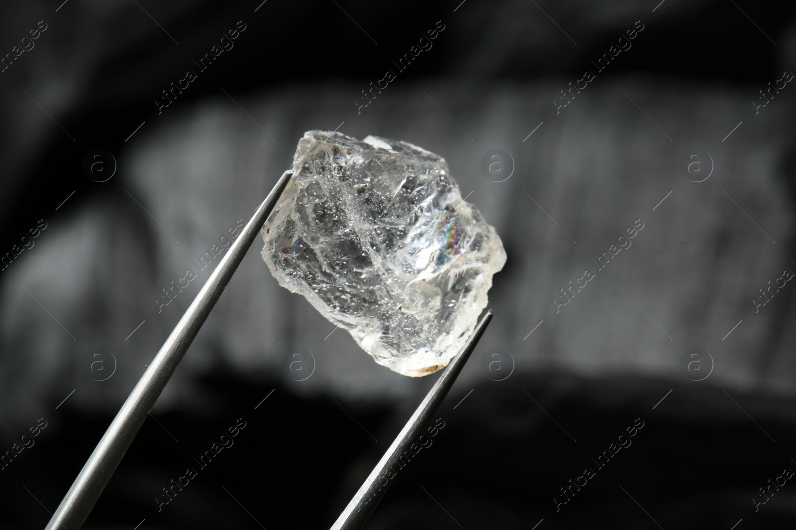 Photo of Tweezers with shiny rough diamond on dark background, closeup