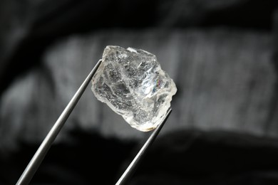 Photo of Tweezers with shiny rough diamond on dark background, closeup