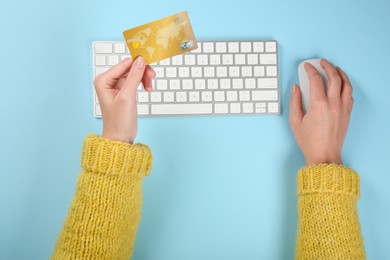 Photo of Online payment. Woman using credit card and computer at light blue table, top view