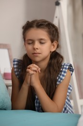 Photo of Cute little girl with hands clasped together praying at home