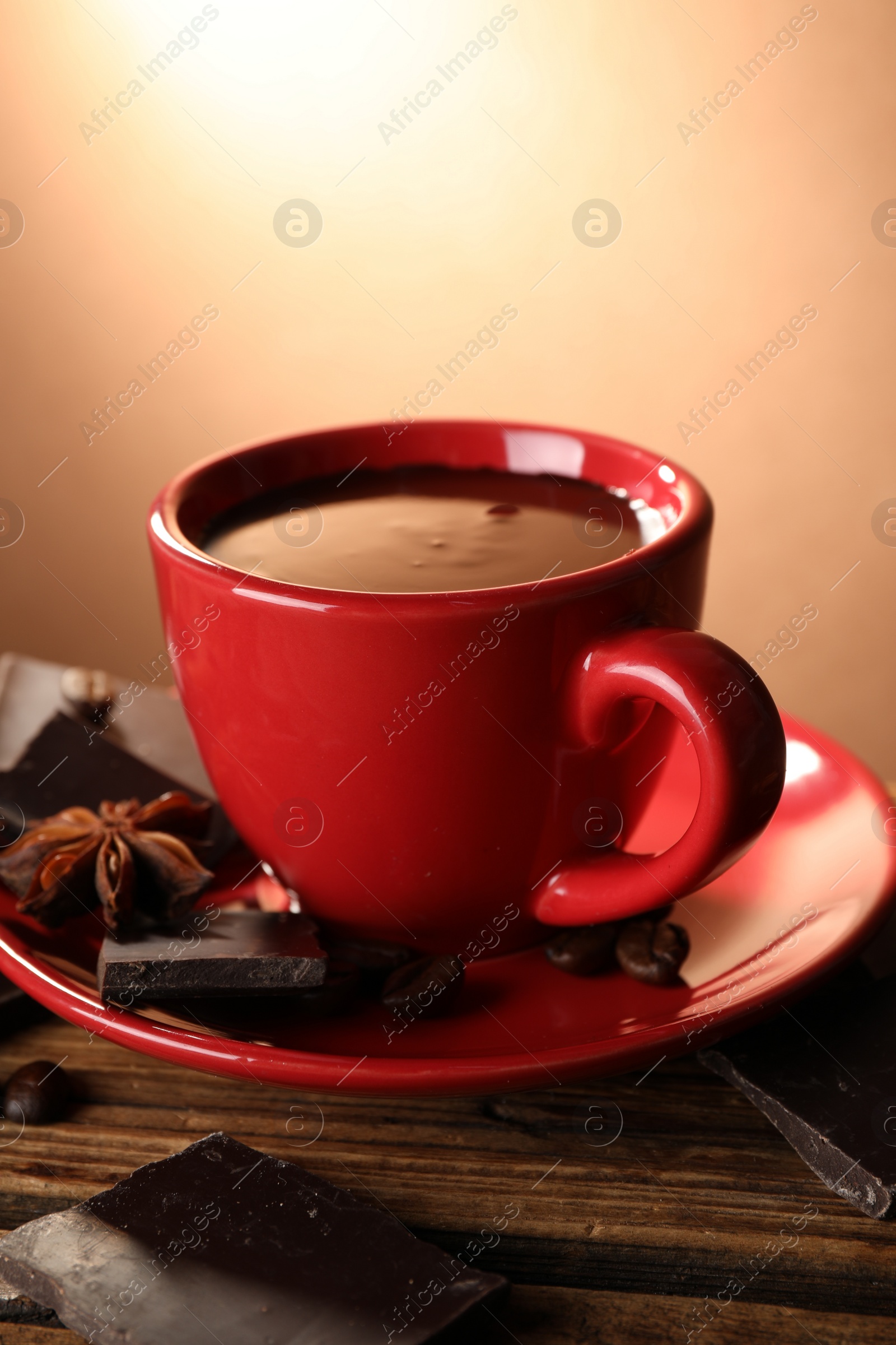 Photo of Cup of delicious hot chocolate, spices and coffee beans on wooden table