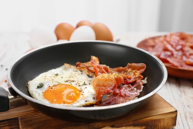 Photo of Frying pan with fried egg and bacon on wooden board, closeup