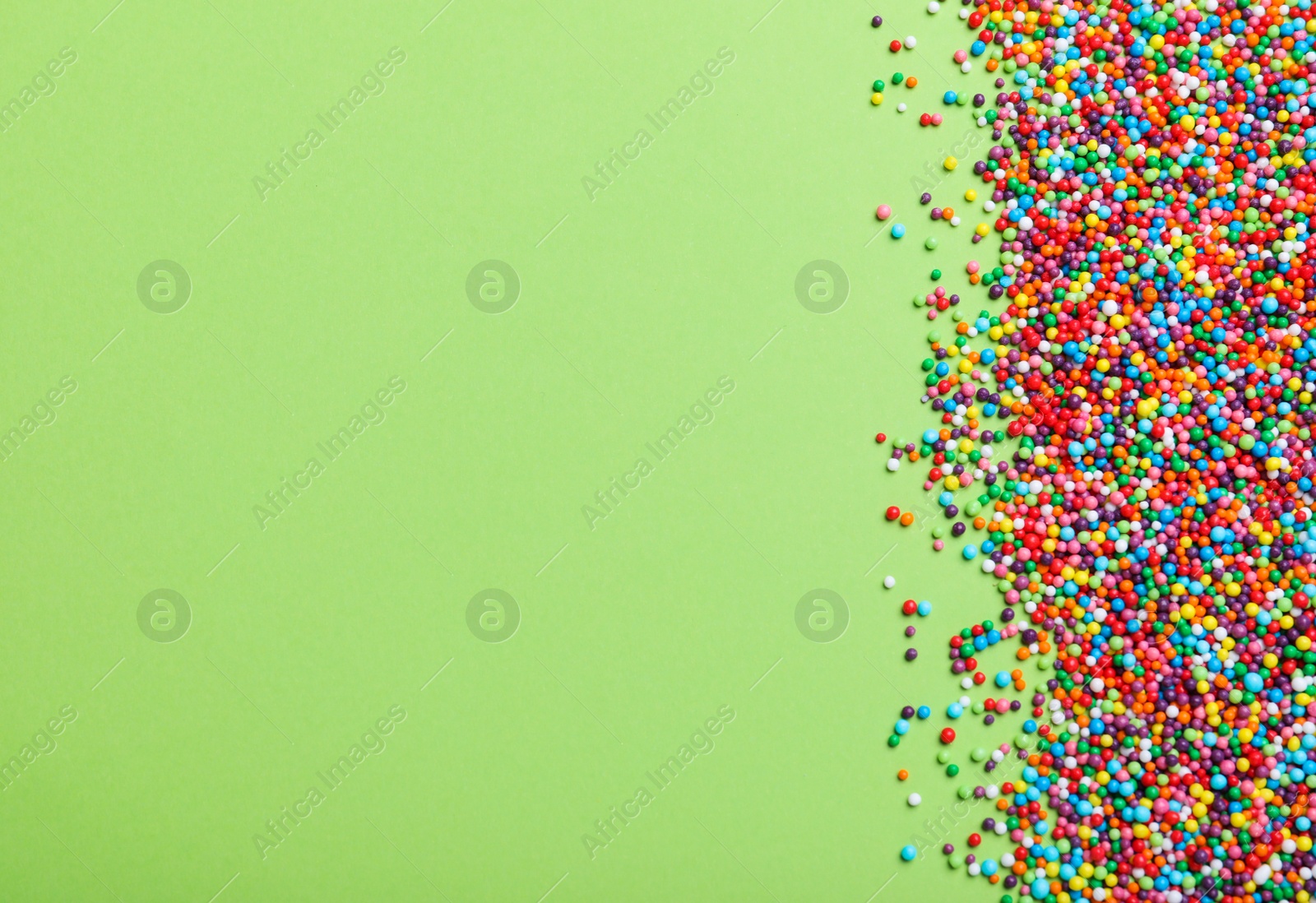 Photo of Colorful sprinkles on green background, flat lay with space for text. Confectionery decor