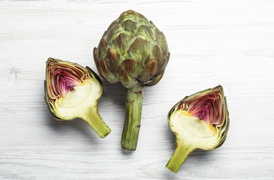 Cut and whole fresh raw artichokes on white wooden table, flat lay
