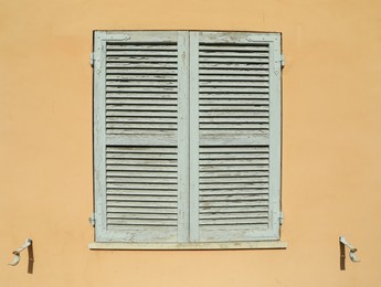 Photo of Window with closed wooden shutters on orange wall