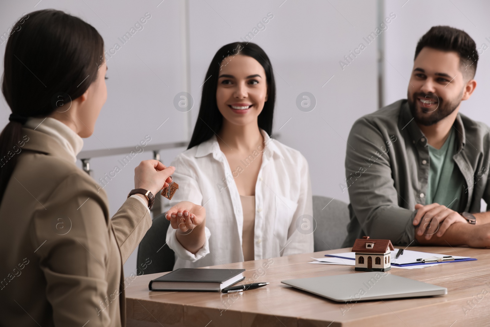 Photo of Real estate agent giving house key to young couple in office, focus on hands. Mortgage concept