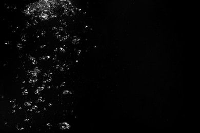 Photo of Air bubbles in water on black background, space for text
