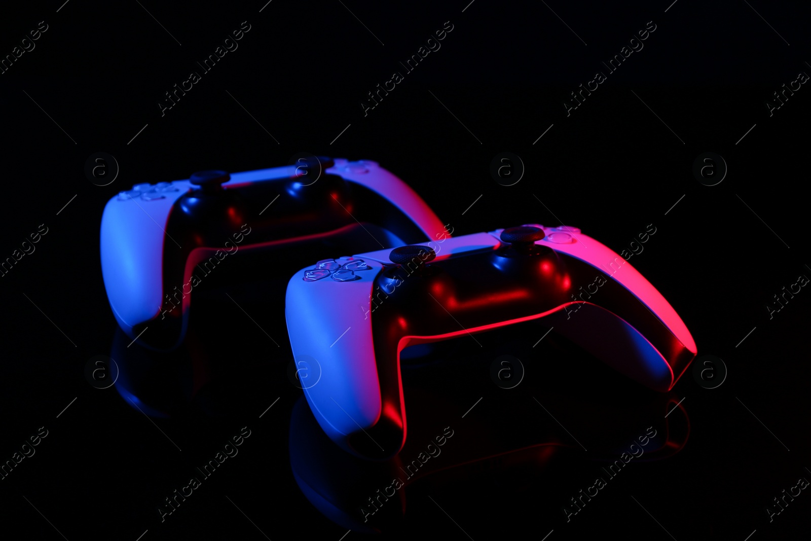 Photo of Wireless game controllers on black mirror surface in neon lights