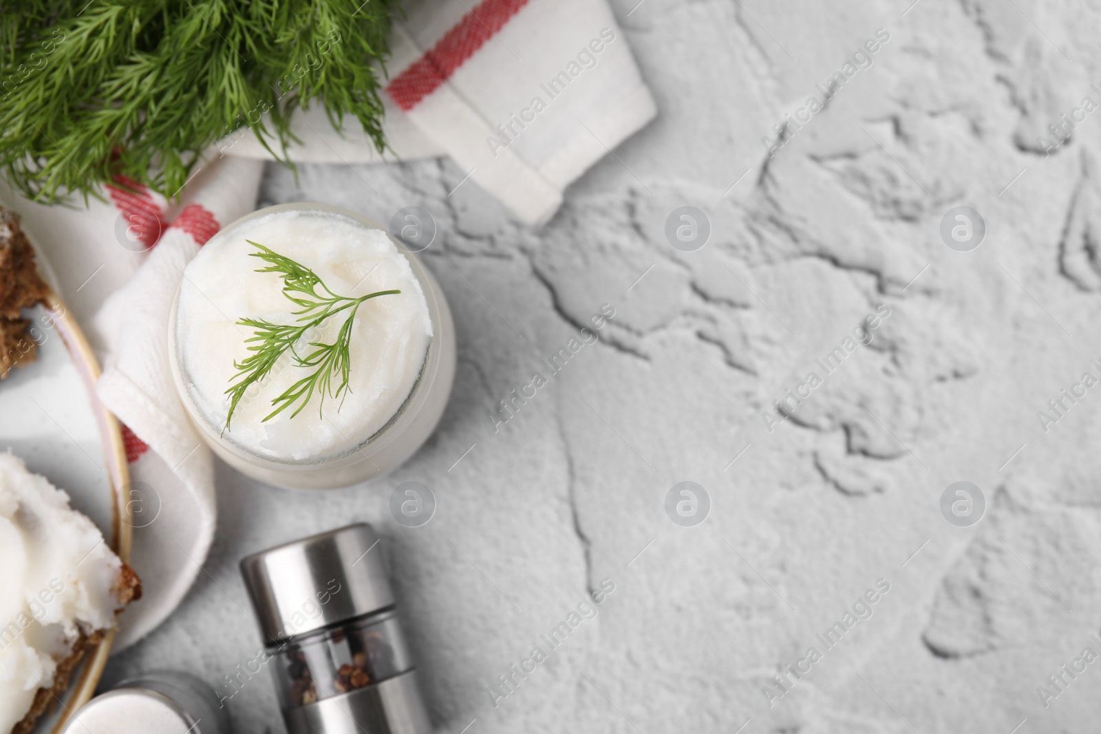 Photo of Delicious pork lard with dill in glass jar and spice shakers on light gray textured table, flat lay. Space for text