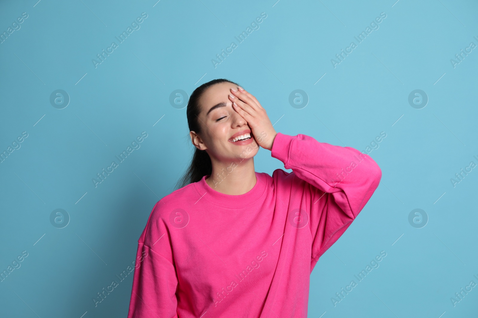 Photo of Beautiful young woman laughing on light blue background. Funny joke