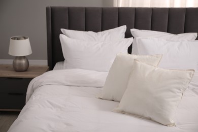 Photo of Many soft white pillows and duvet on bed indoors