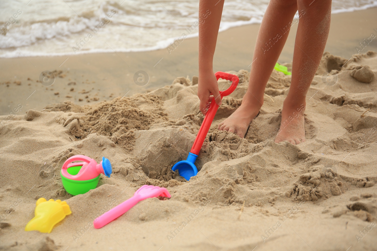 Photo of Little girl playing with plastic toys on sandy beach, closeup