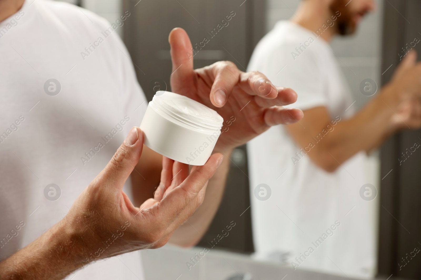 Photo of Handsome man applying cream in bathroom, closeup