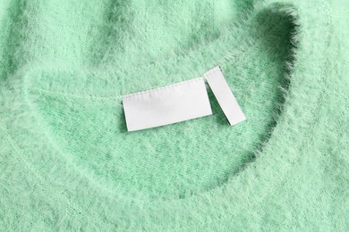 Photo of Blank clothing label on light green sweater, top view