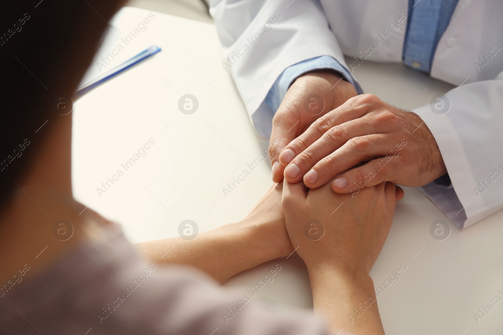 Photo of Male doctor comforting woman at table, closeup of hands. Help and support concept