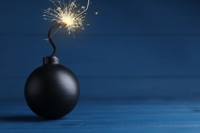 Image of Old fashioned black bomb with lit fuse on blue wooden table, space for text
