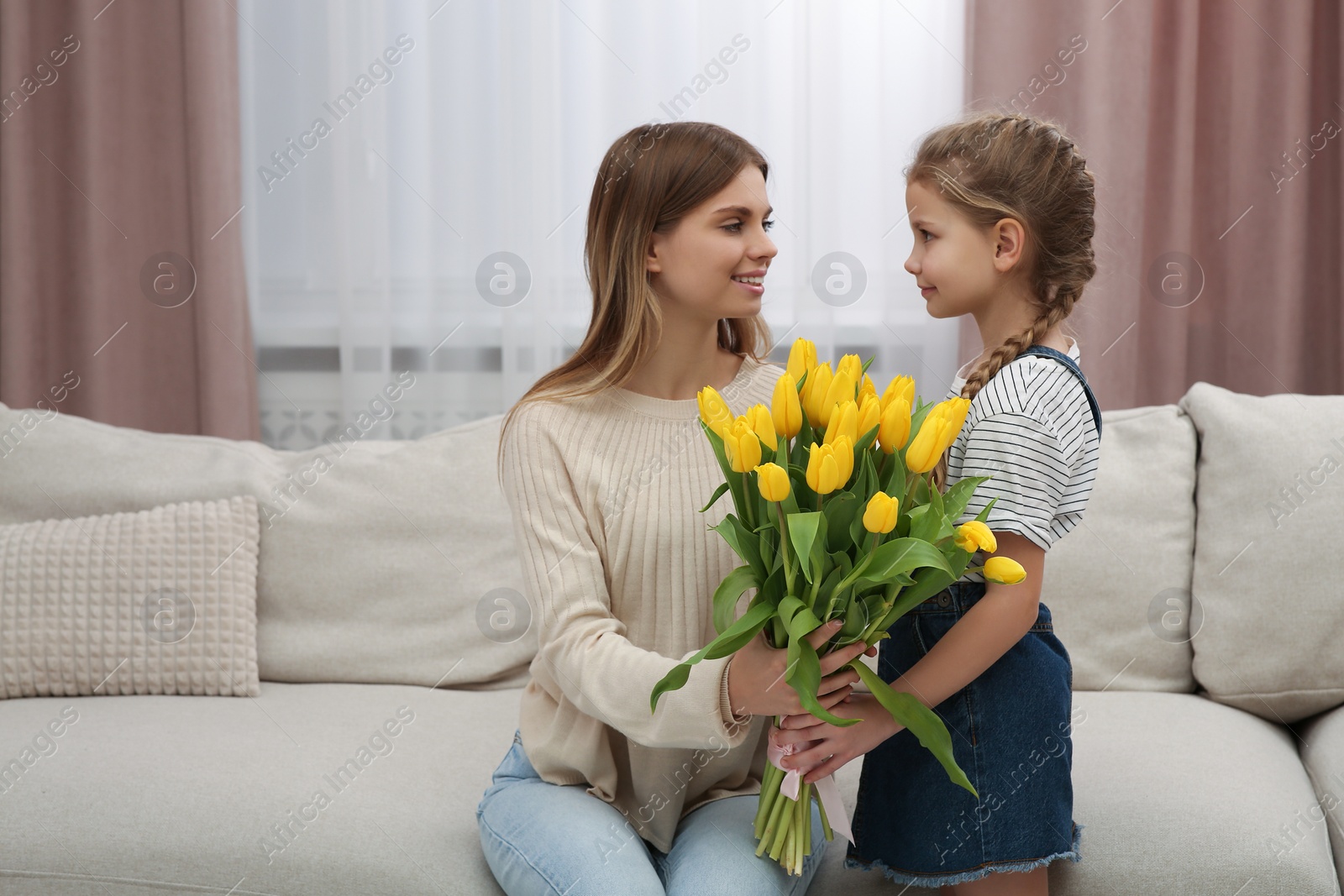 Photo of Little daughter congratulating mom with bouquet of yellow tulips at home. Happy Mother's Day