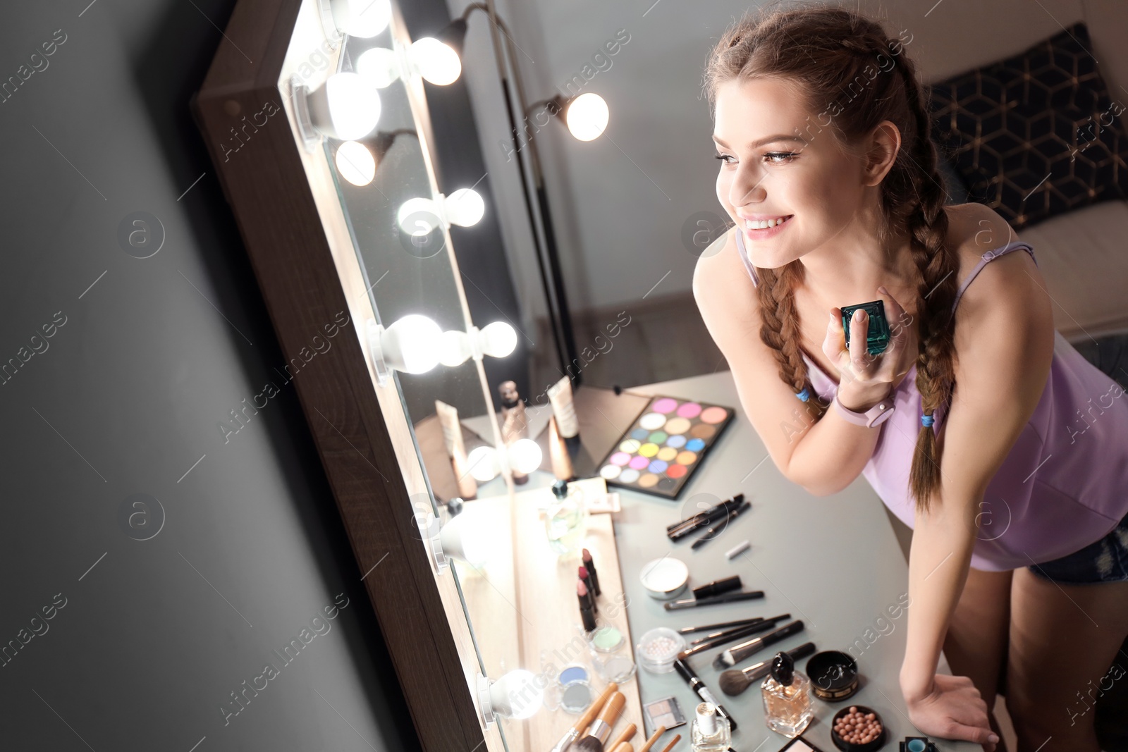 Photo of Portrait of beautiful woman with natural makeup applying perfume near mirror indoors