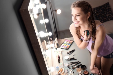 Photo of Portrait of beautiful woman with natural makeup applying perfume near mirror indoors