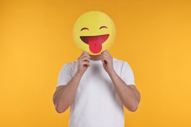 Photo of Man covering face with emoticon sticking out tongue on yellow background