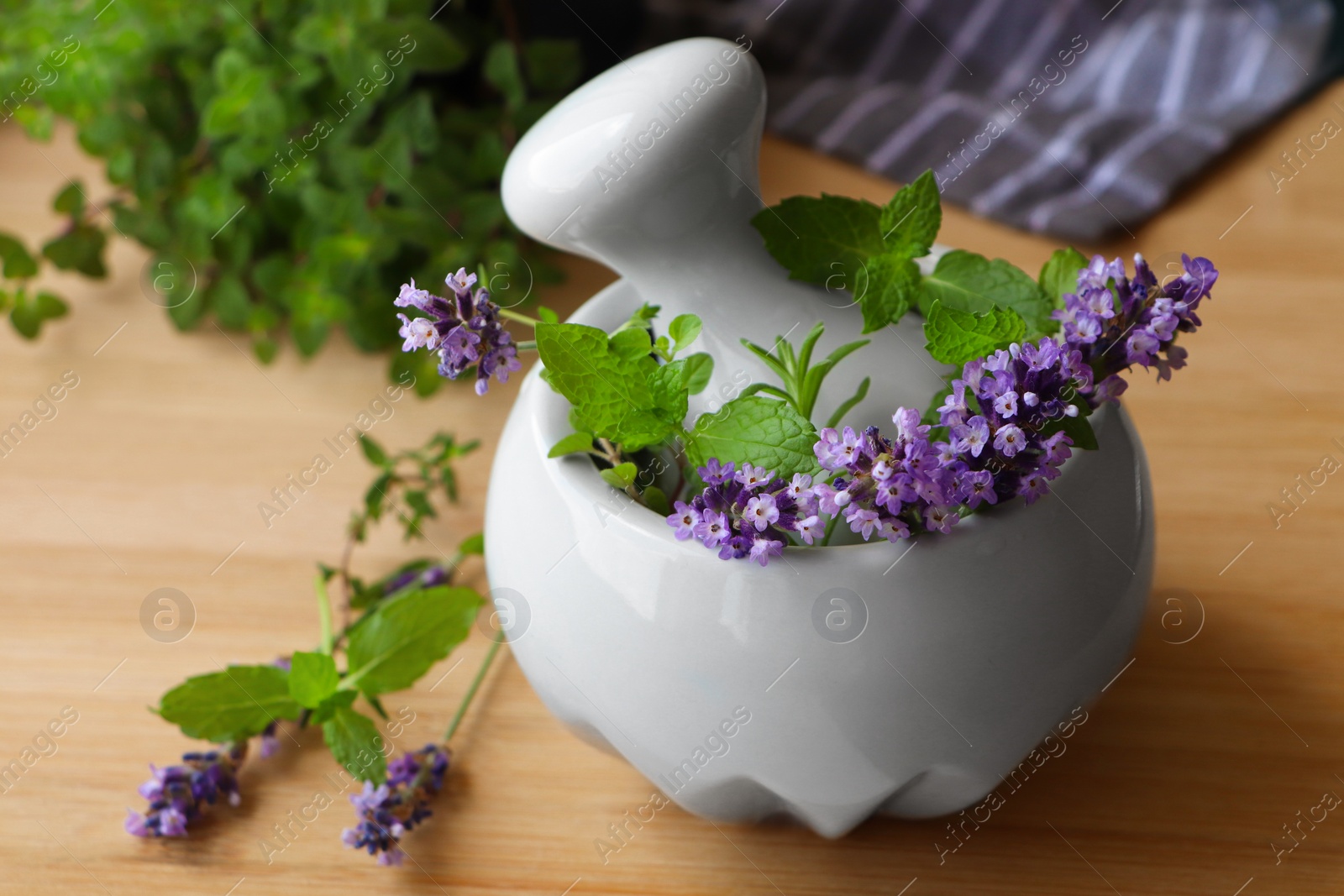 Photo of Mortar with fresh lavender flowers, herbs and pestle on wooden table