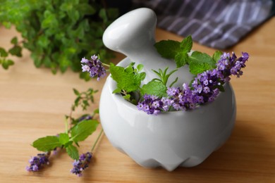 Photo of Mortar with fresh lavender flowers, herbs and pestle on wooden table