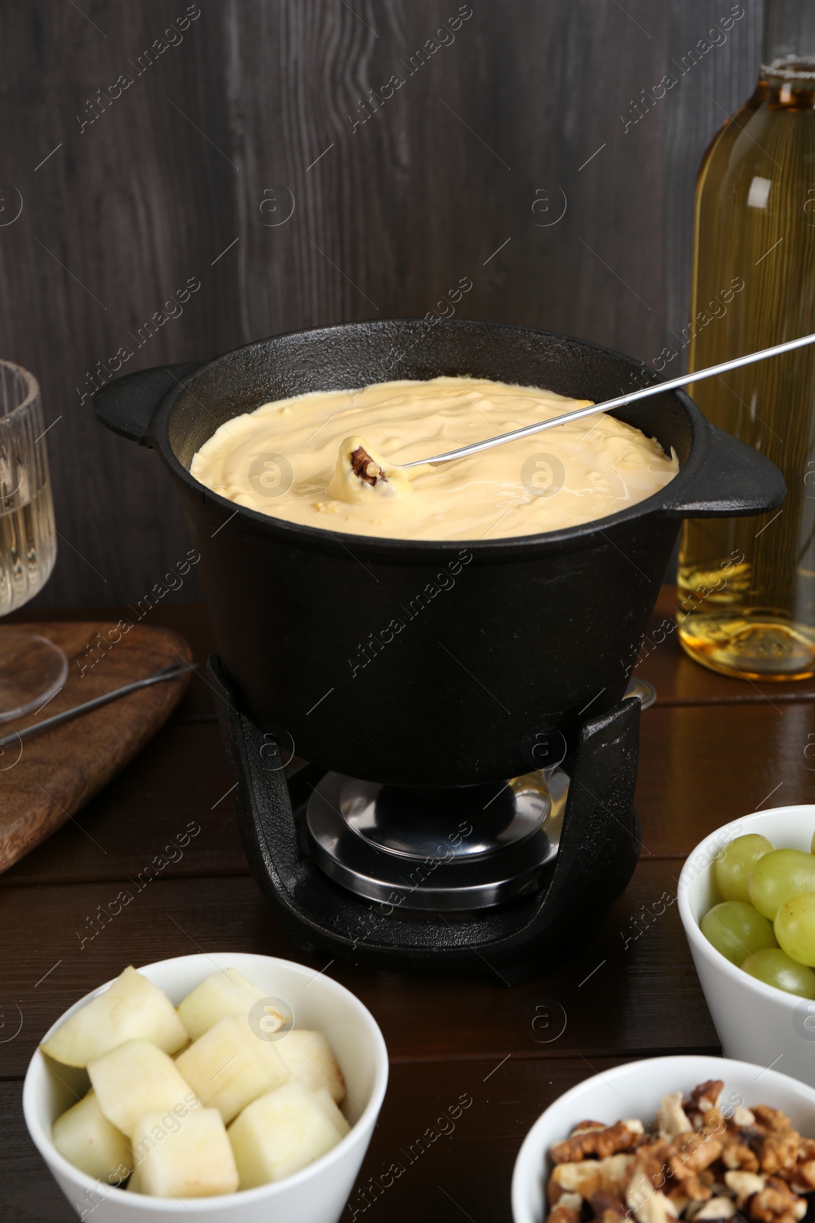 Photo of Fondue pot with tasty melted cheese, fork, wine and different snacks on wooden table