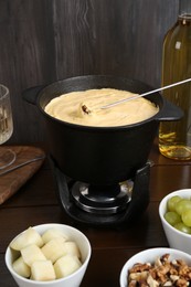 Fondue pot with tasty melted cheese, fork, wine and different snacks on wooden table
