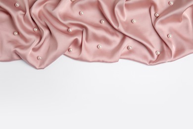 Texture of delicate pink silk with pearls on white background, top view