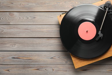 Turntable with vinyl record on grey wooden background, top view. Space for text