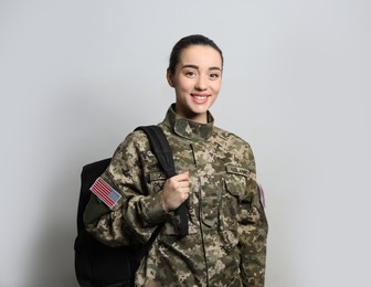 Photo of Female soldier with backpack on light grey background. Military education