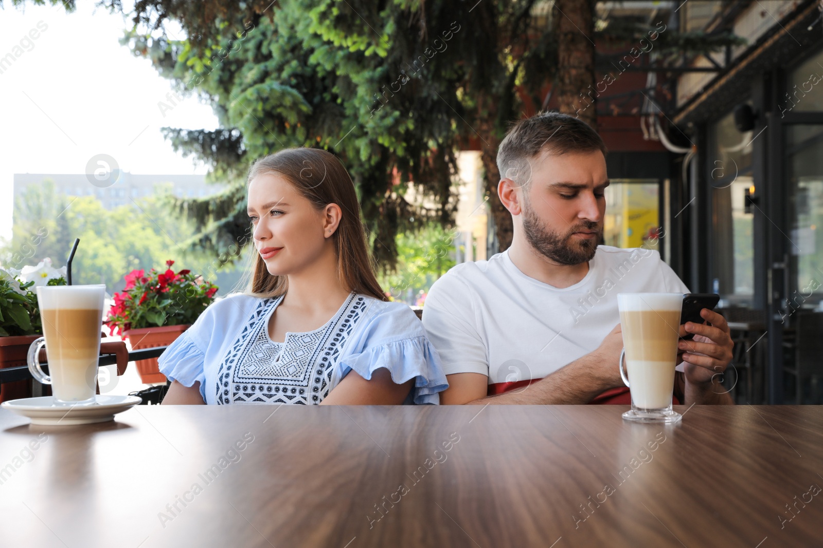 Photo of Young man with smartphone ignoring his girlfriend in outdoor cafe. Boring date