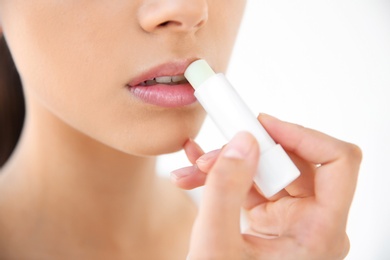 Photo of Young woman applying balm on her lips against light background, closeup