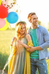 Young couple with colorful balloons in field on sunny day