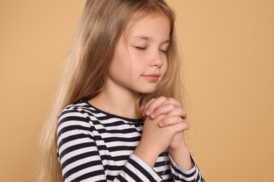 Photo of Girl with clasped hands praying on beige background